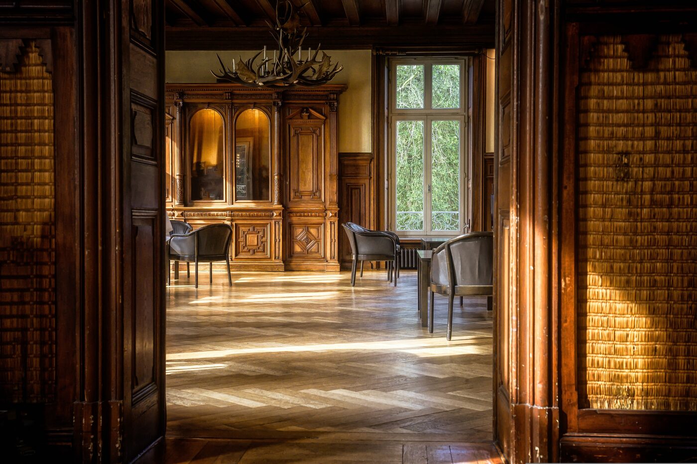 Historischer holzgetäfelter Salon mit Geweihkronleuchter, antikem Schrank und Parkettboden
