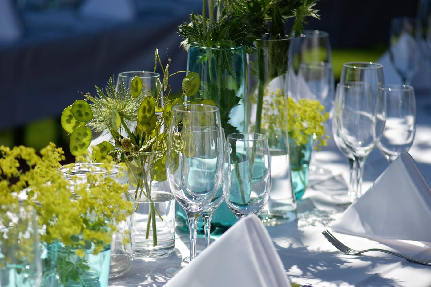 Festlich gedeckte Gartentafel mit Weingläsern, Kerzen und frischen Blumen in türkisen Vasen